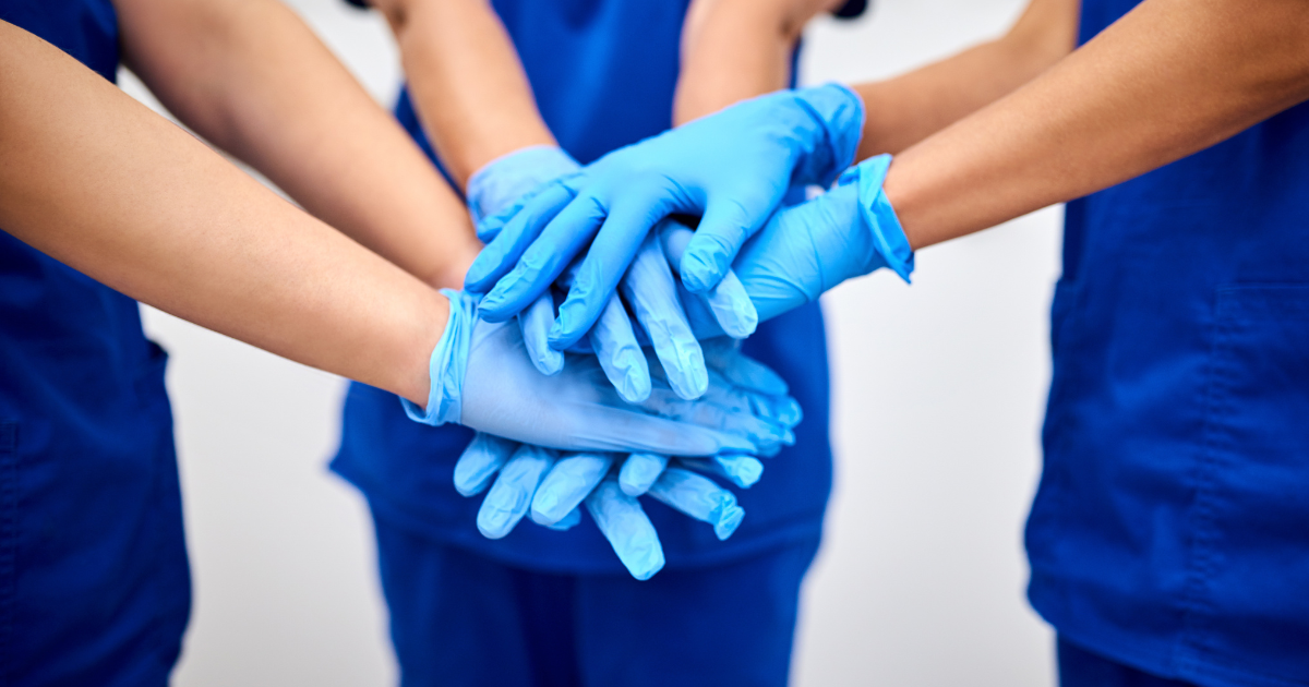Nurses in a clinical setting putting their hands together in a team huddle, representing collaboration in wound care practice.